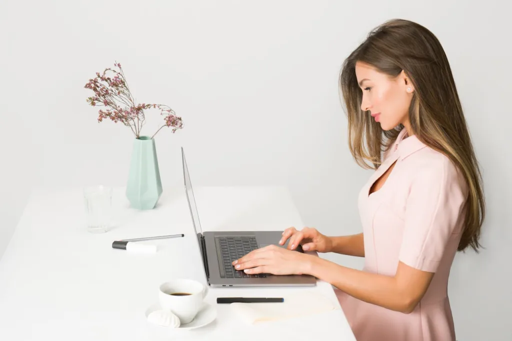 mulher branca com cabelos longos de perfil na frente de um computador, digitando